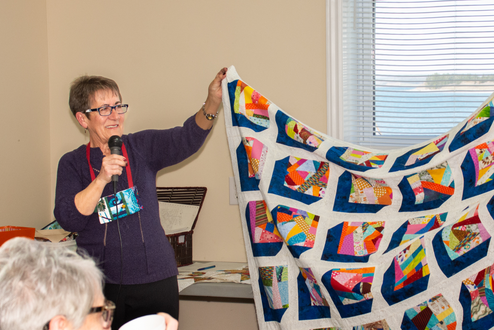 Woman holding up one end of a quilt while talking over a microphone